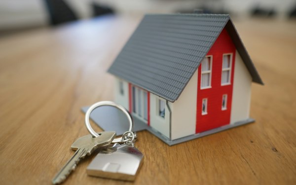 Set of keys beside a small model house on a wooden table, ownership concept
